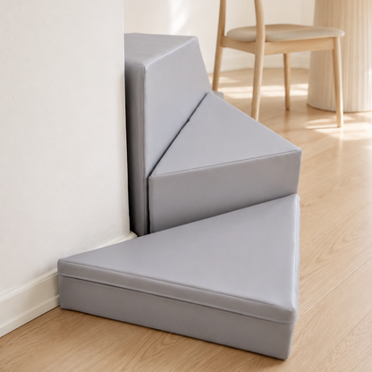 Gray soft blocks placed around a corner in a room with wooden flooring and a dining table.