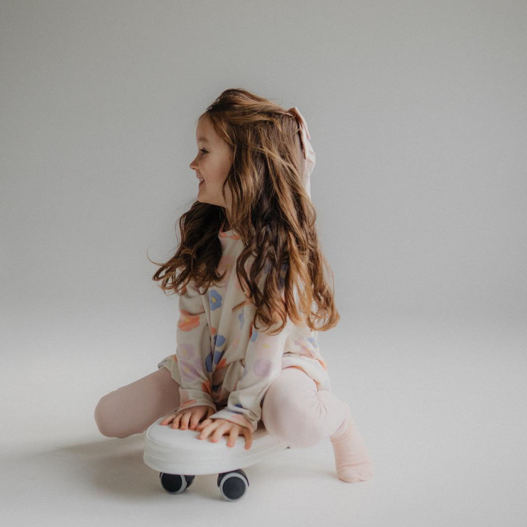 Young girl sitting on a white soft ride on toy against a plain background